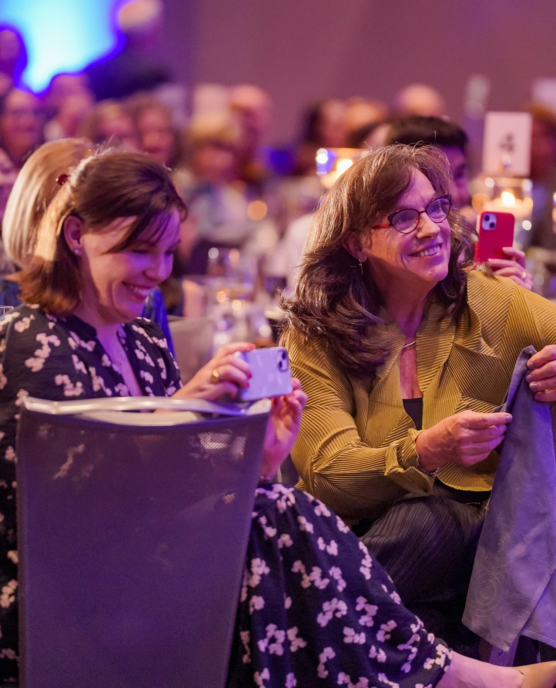 Two women sitting at a table at a gala smiling